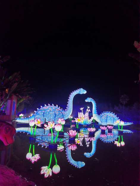 Illuminated dinosaur forms, reflected light, scenic plants, color and atmosphere reshape the visitor route after dark.